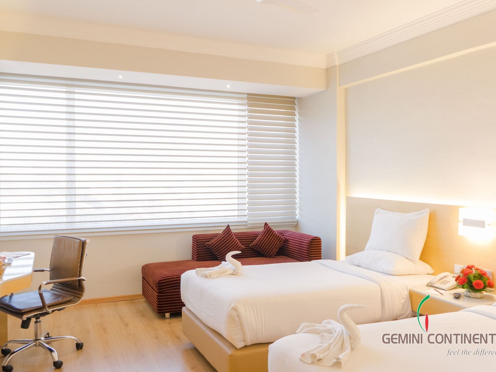 A room featuring twin beds, a seating area, desk, and chair at Gemini Continental.