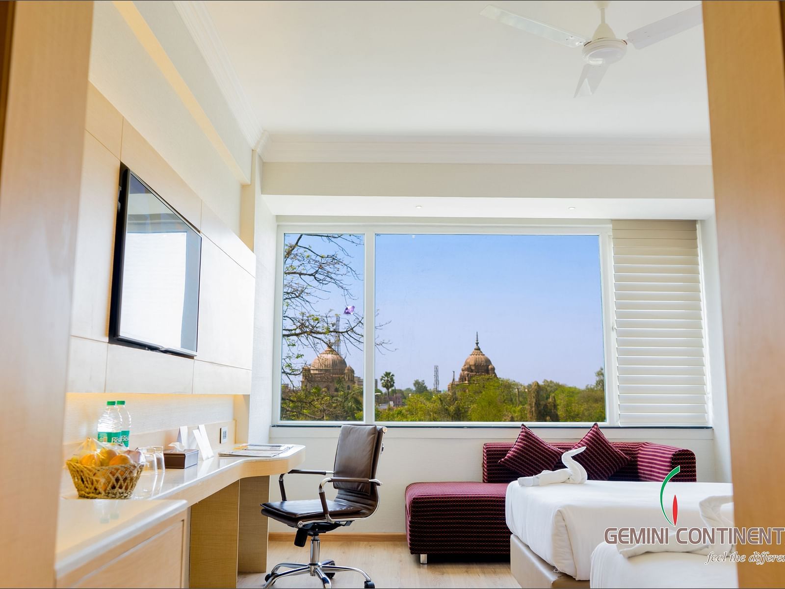 An entrance view of a room with a desk, twin beds, chair, seating area, and a huge window | Gemini Continental