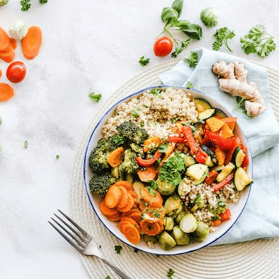 A colorful plate of healthy food with brown rice, sautéed vegetables, and herbs, surrounded by fresh ingredients on a white surface.