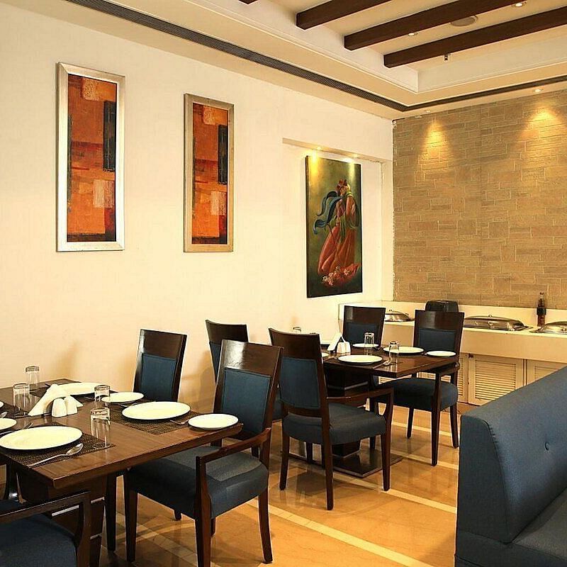 Tables and chairs neatly arranged with cutlery set on the table at Café Inde, Inde Signature Tower, Gurgaon