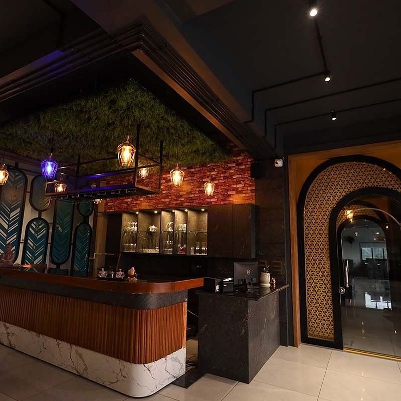 The image shows a bar area with stools, hanging lights, and decorative elements in a dimly lit setting - Lords Eco Inn Navsari.
