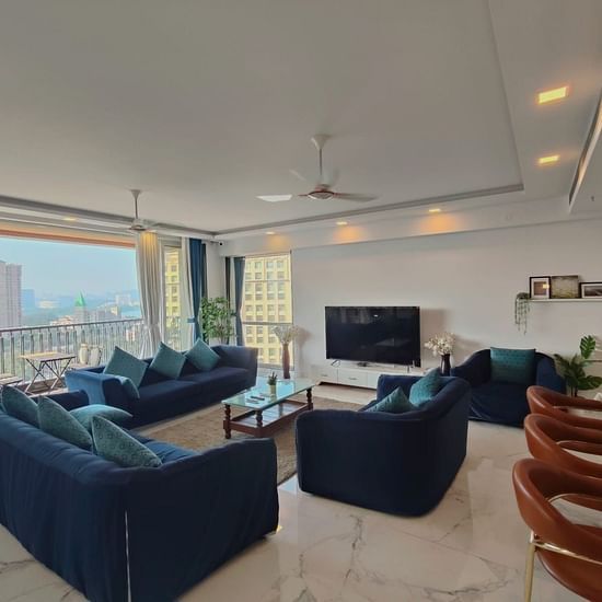1hall and living room area of Maxxvalue Hotel, Chitranjan Tower, Powai with blue themed couch and a dining table in the corner of the room