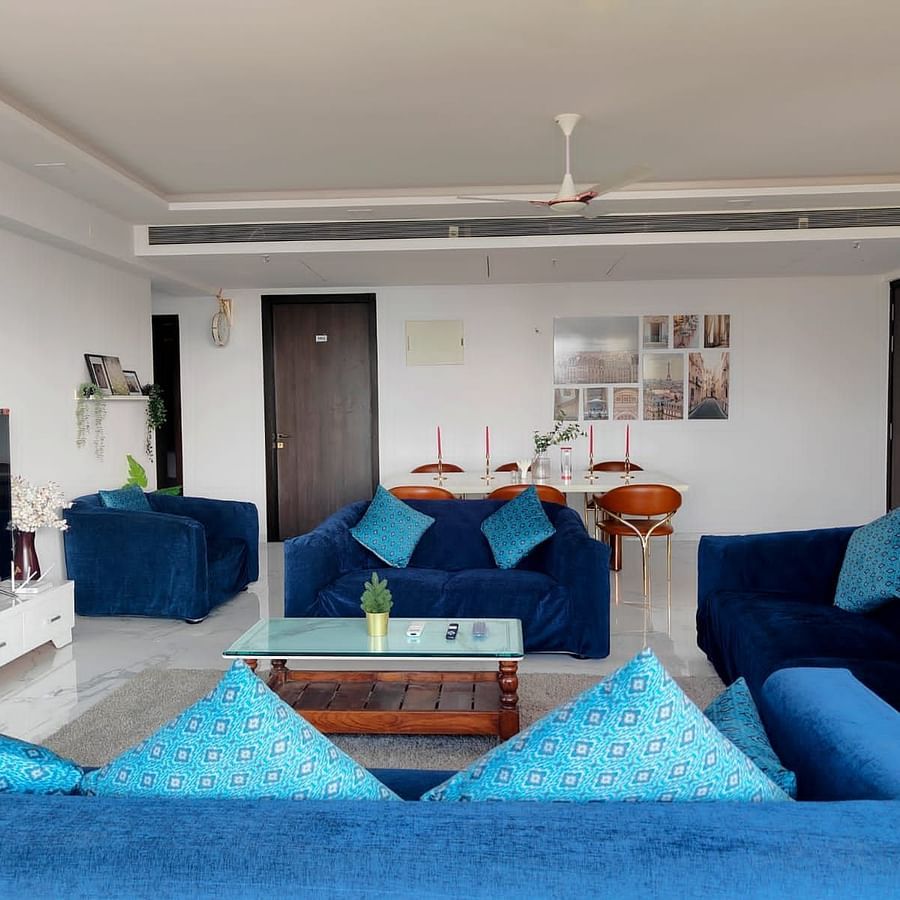 3hall and living room area of Maxxvalue Hotel, Chitranjan Tower, Powai with blue themed couch and a dining table in the corner of the room