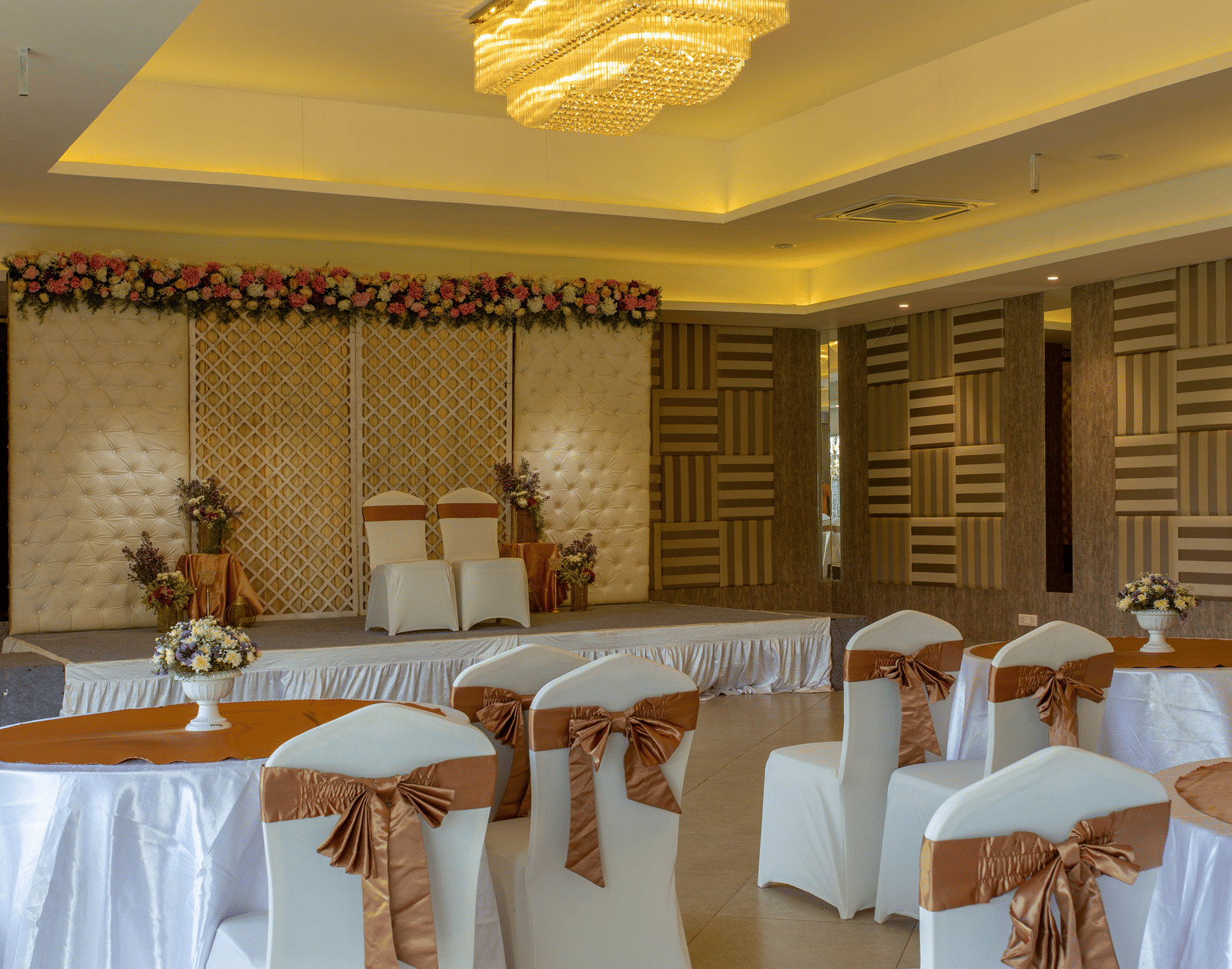 A brightly lit indoor banquet hall or reception area with tables and chairs set up, featuring elegant decor and a patterned wall - Grande Bay Resort & Spa, Mamallapuram