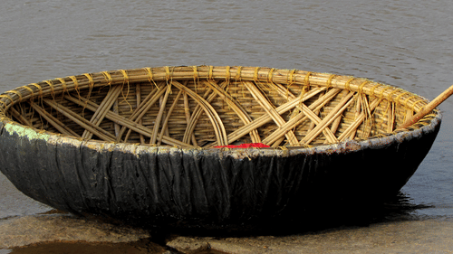 A close up of a Coracle boat with an oar kept inside it, floating on a waterbody near a step. These coracle rides provide opportunities to visit the many places to see in Kabini.