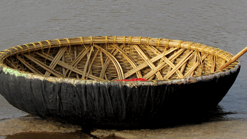 A close up of a Coracle boat with an oar kept inside it, floating on a waterbody near a step. These coracle rides provide opportunities to visit the many places to see in Kabini.