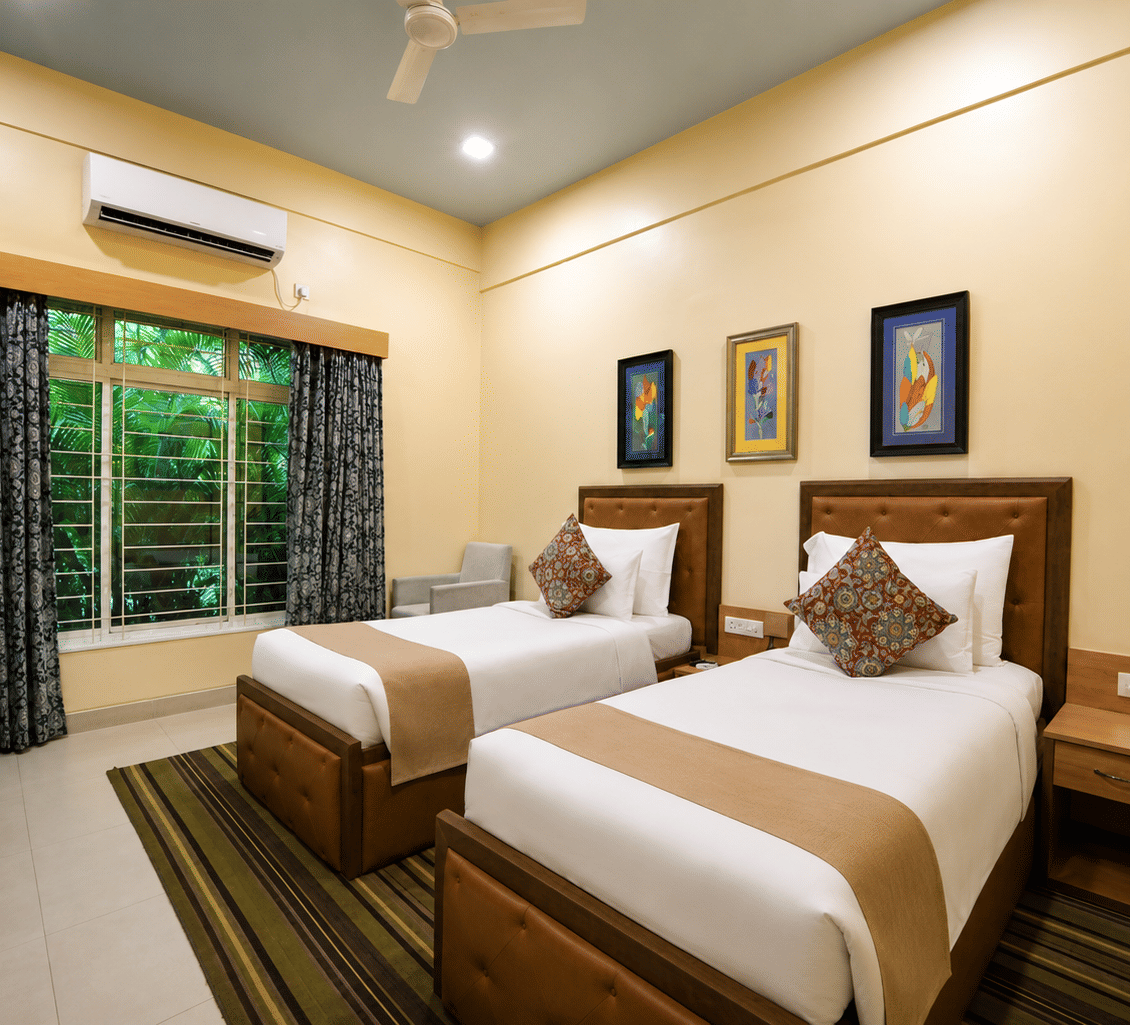 Executive room with two single beds, tan leather headboards, framed artwork, a work desk, chair and a striped rug at MAYFAIR World Cup Village, Rourkela.
