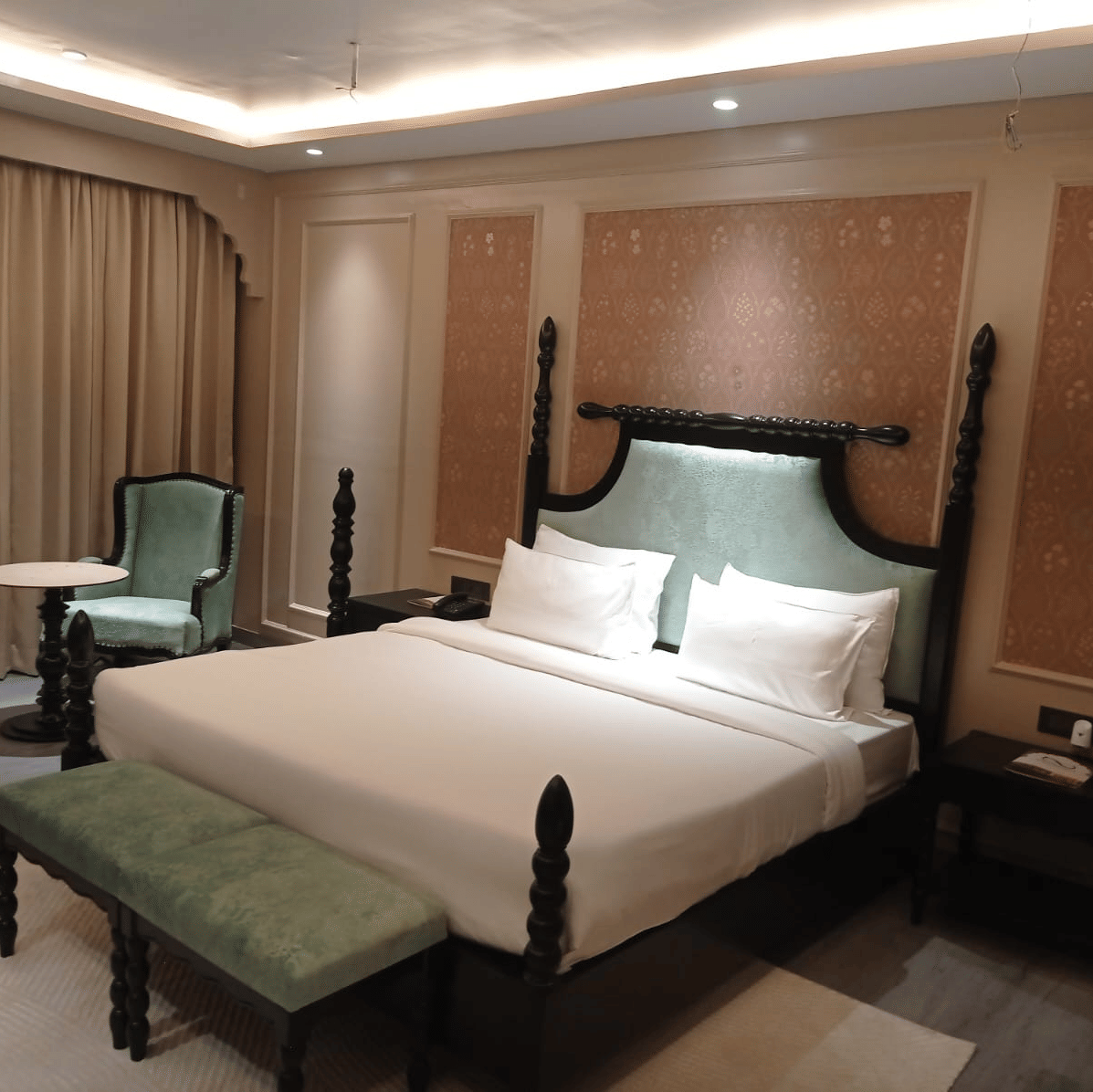 Bedroom with king size bed, side tables, chairs and window curtain at Beelwa Palace, Jaipur