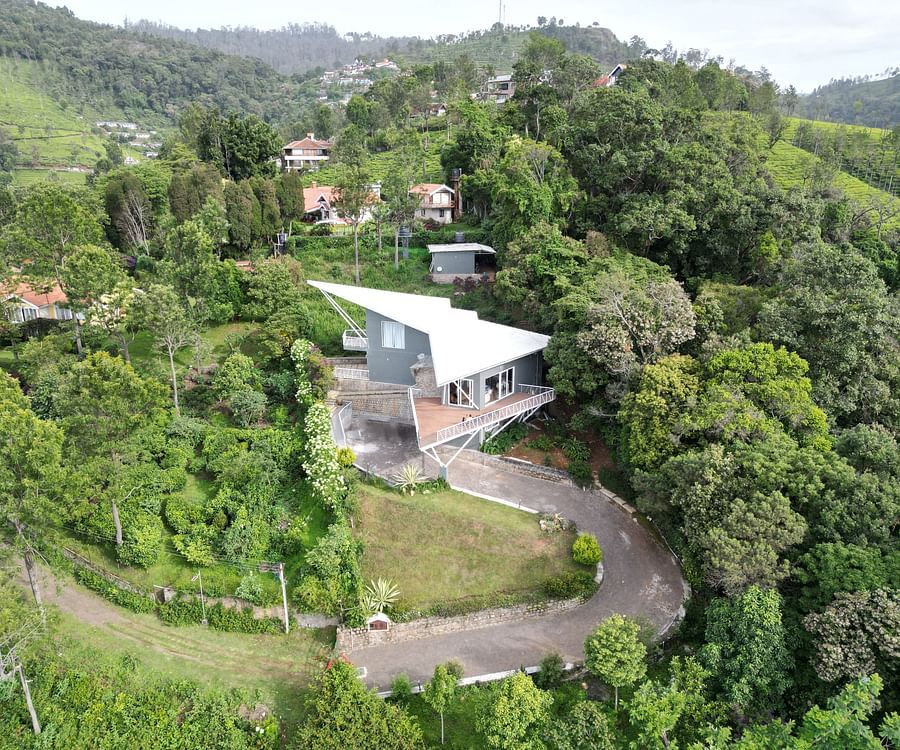Elevated view of a house set against forested hills under a cloudy sky at Ibex Resorts, Coonoor (Tapas).