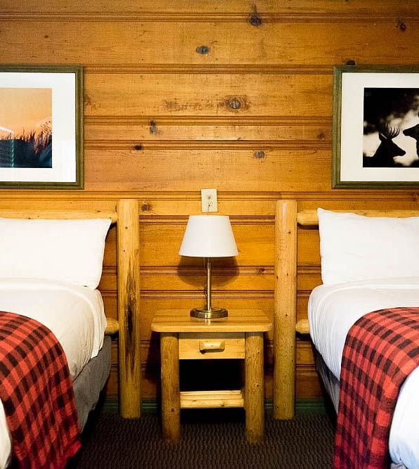 A wooden cabin with twin beds and a side table with a night lamp placed between them at Shaver Lake Village Hotel.