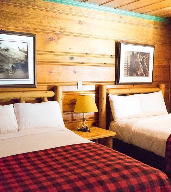 A wooden cabin with twin beds with photographs hung on the wall behind them at Shaver Lake Village Hotel.