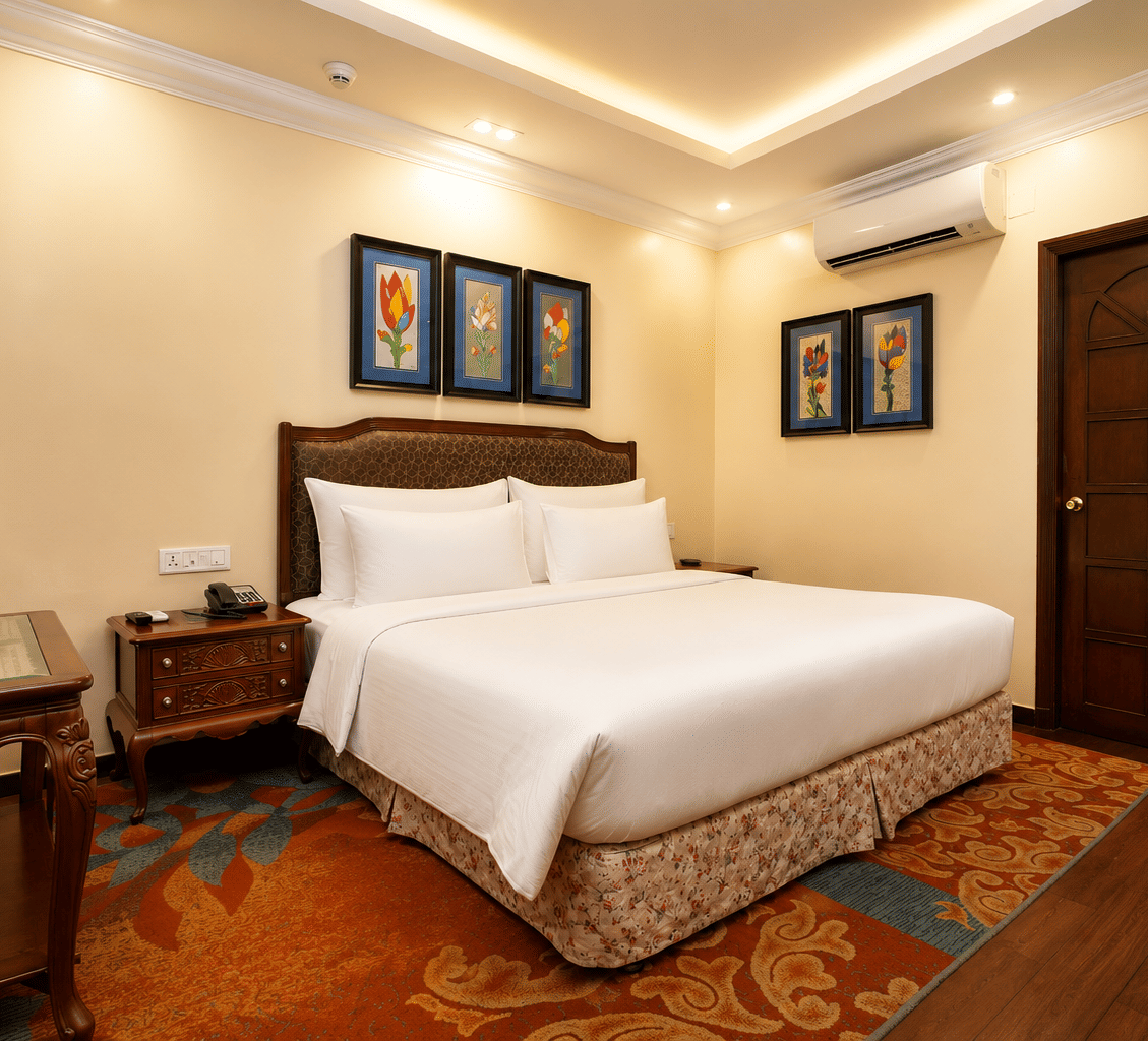Executive room with a king bed, upholstered headboard, framed floral prints, bedside telephone, writing desk and a patterned carpet at MAYFAIR Garden, Rourkela.