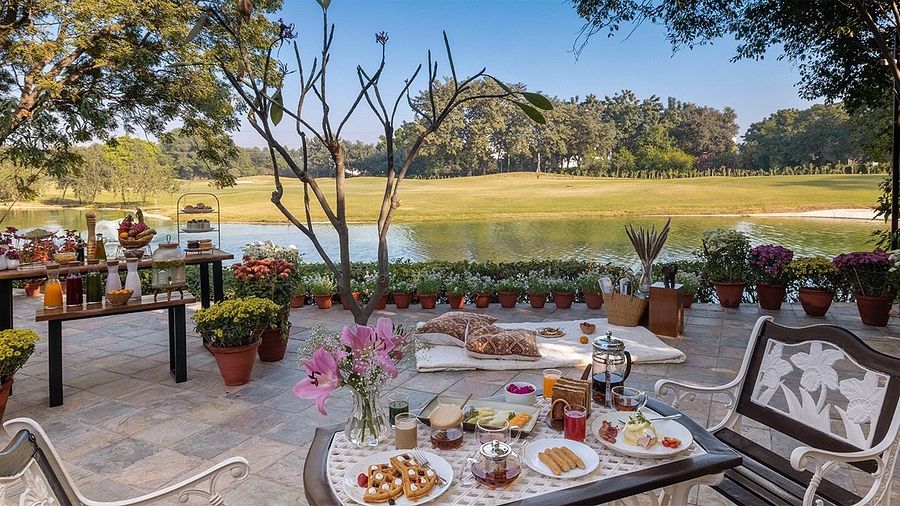 Outdoor dining setup with multiple tables and food spread under trees, overlooking an open green field at Karma Chalets.