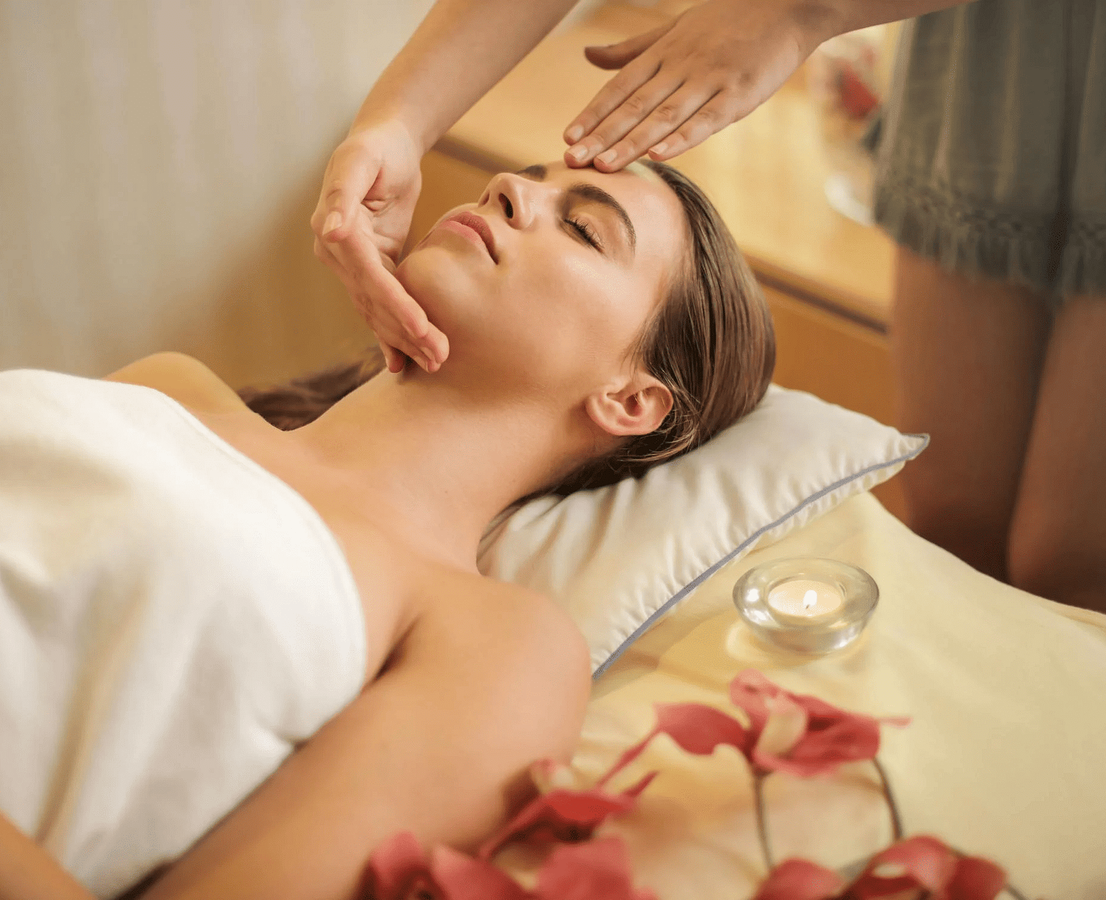 Woman wrapped in a towel lying on a bed and getting a massage.