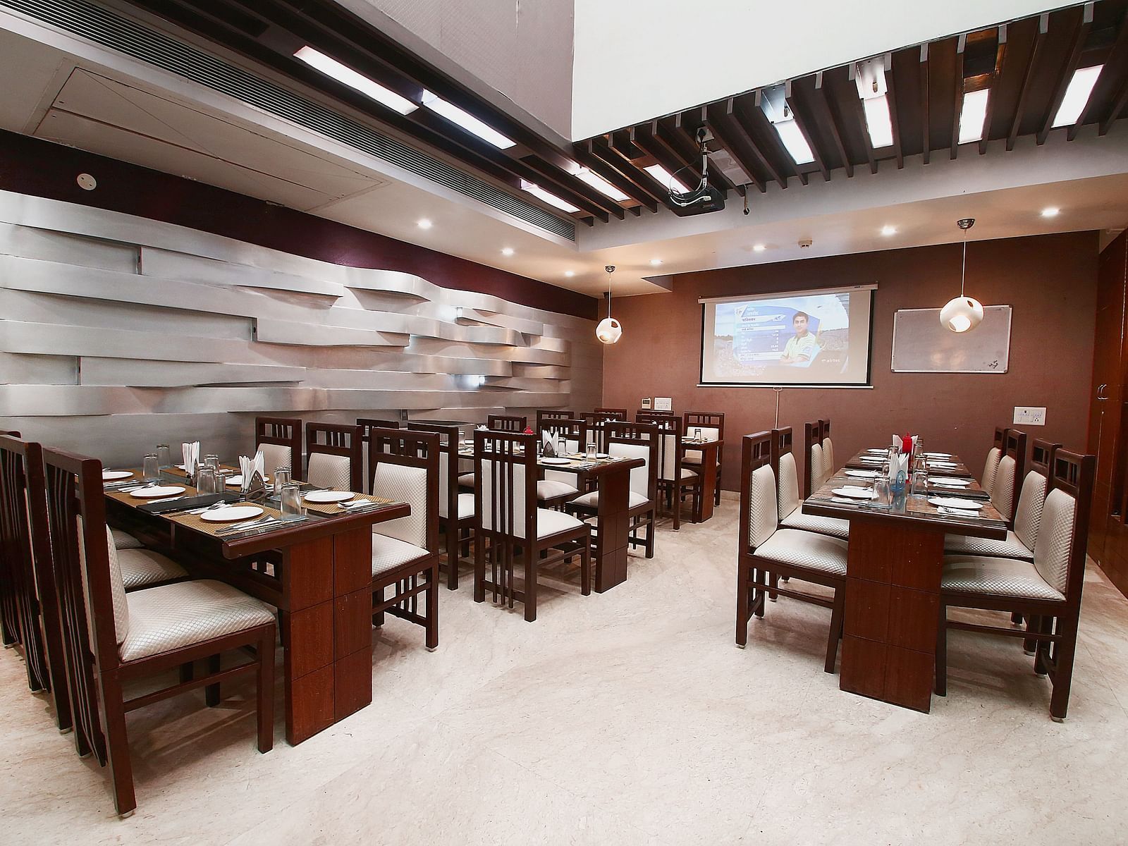 Modern dining space with various tables and chairs for guests to sit in and dine along with beautiful textured patterns on the wall and ambient  lighting - Hotel Emerald, Chandigarh