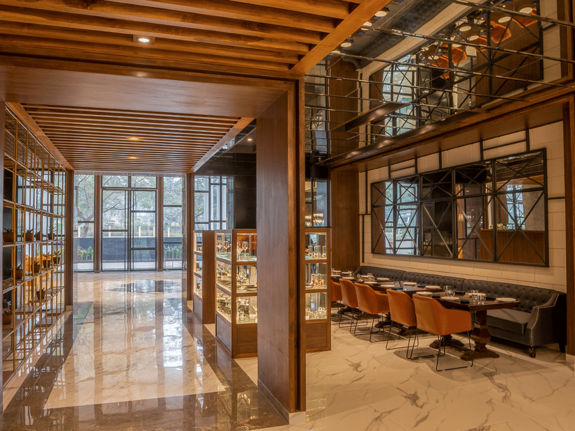 Restaurant entryway with marble floor, wine display, banquette seating and orange leather chairs at Polo Hotel, Agartala.