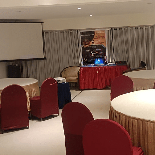 Professional banquet hall at Lords Eco Inn Dahej with round tables, burgundy chairs, and presentation screen for events and conferences