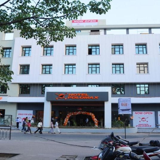 alt-text Exterior of Hotel Polo Max during the daytime with clear view of entrance and side coaching institute banners.