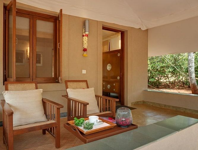 A living room with a couch, chairs, and a view of a garden - Shreyas Retreat