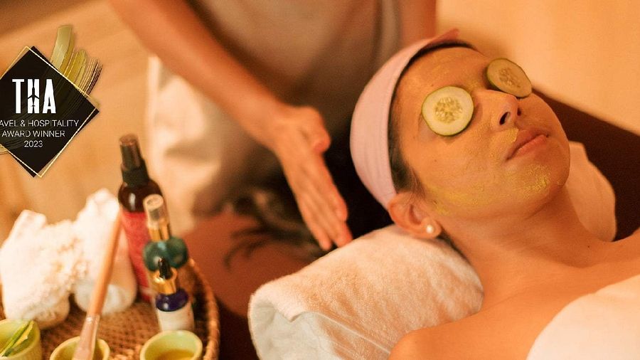 Person receiving a facial treatment with cucumber slices on eyes; massage oils and towels displayed at Karma Chalets.