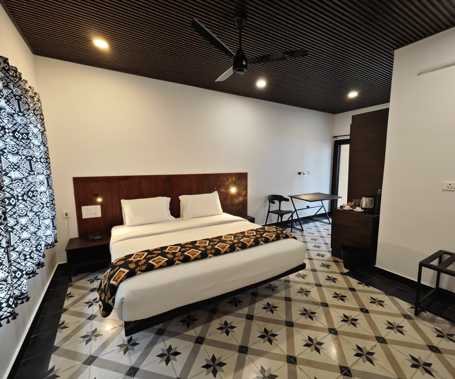 Modern guest room interior with a king size bed, decorative floor tiles, and dark wood ceiling accents - Ibex Resorts, Malampuzha (Kava Eco Camp and Caravan Park)