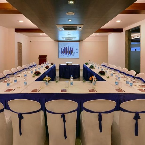 A long conference table with chairs, water bottles, and presentation materials in a meeting room with a projector screen.