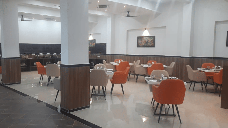 A brightly lit dining area features numerous tables with orange chairs - Kankidham Lords Inn