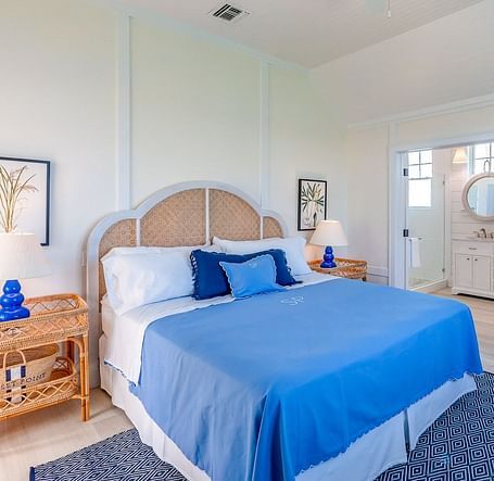 Bright bedroom with a woven headboard, blue bedding, wooden furniture, and framed botanical wall art | Abaco Inn