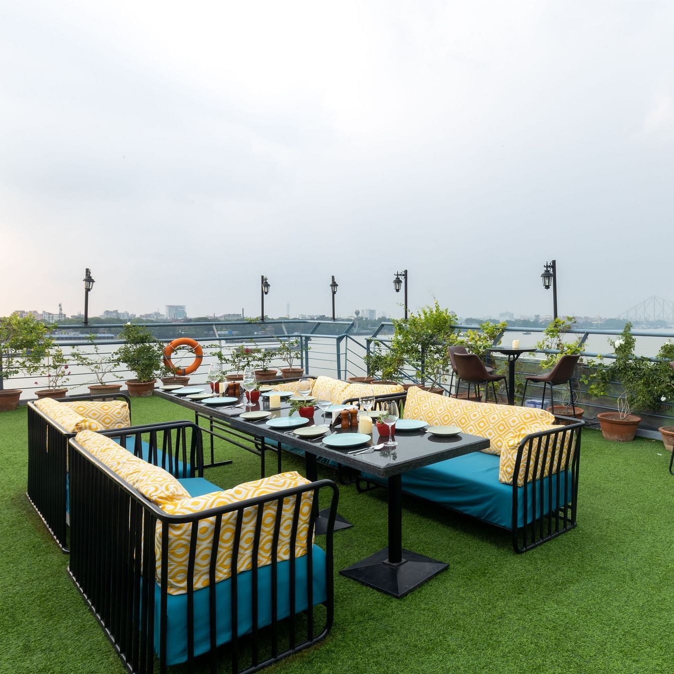  An outdoor dining setup on a rooftop garden overlooking a bridge and river during daylight - Polo Floatel