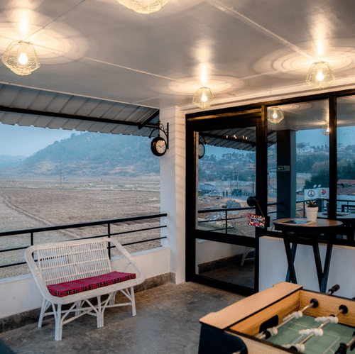 Covered balcony lounge at Woodstock Resort with seating, a foosball table, hanging lights, and large windows overlooking hills and an open landscape.