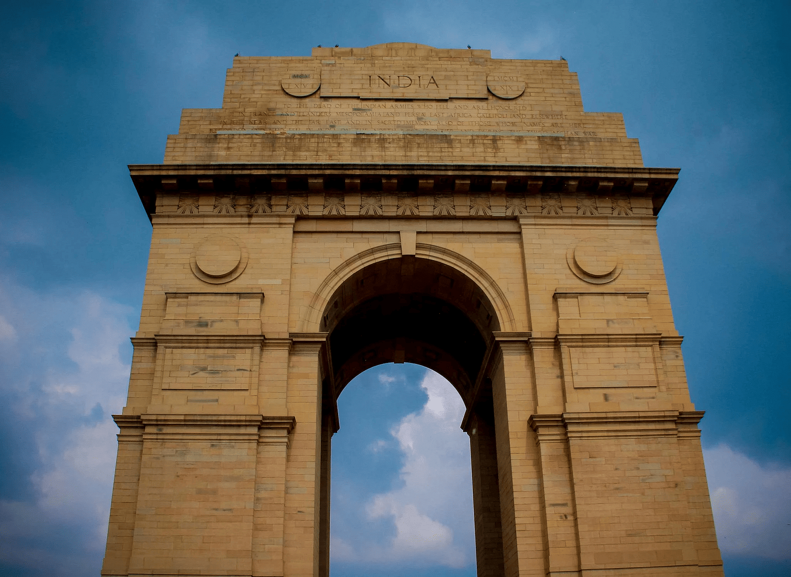 Image of India Gate with cloudy blue sky in the background.