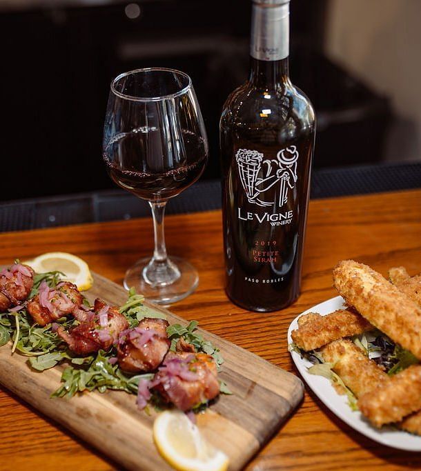 Two dishes being served alongside a bottle of red wine on a wooden table - Narrow Gauge Inn - A Serenite Hotel Near Fish Camp.