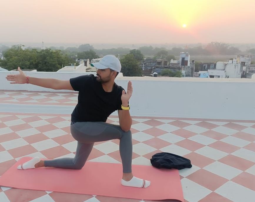 A person performs a yoga pose on a mat on a rooftop with a sunrise or sunset in the background.