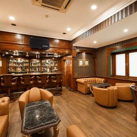 Cavalry Bar with backlit bottle shelves, carved wooden stools, tan leather seating, marble-topped tables and wood panelling at MAYFAIR Garden, Rourkela.