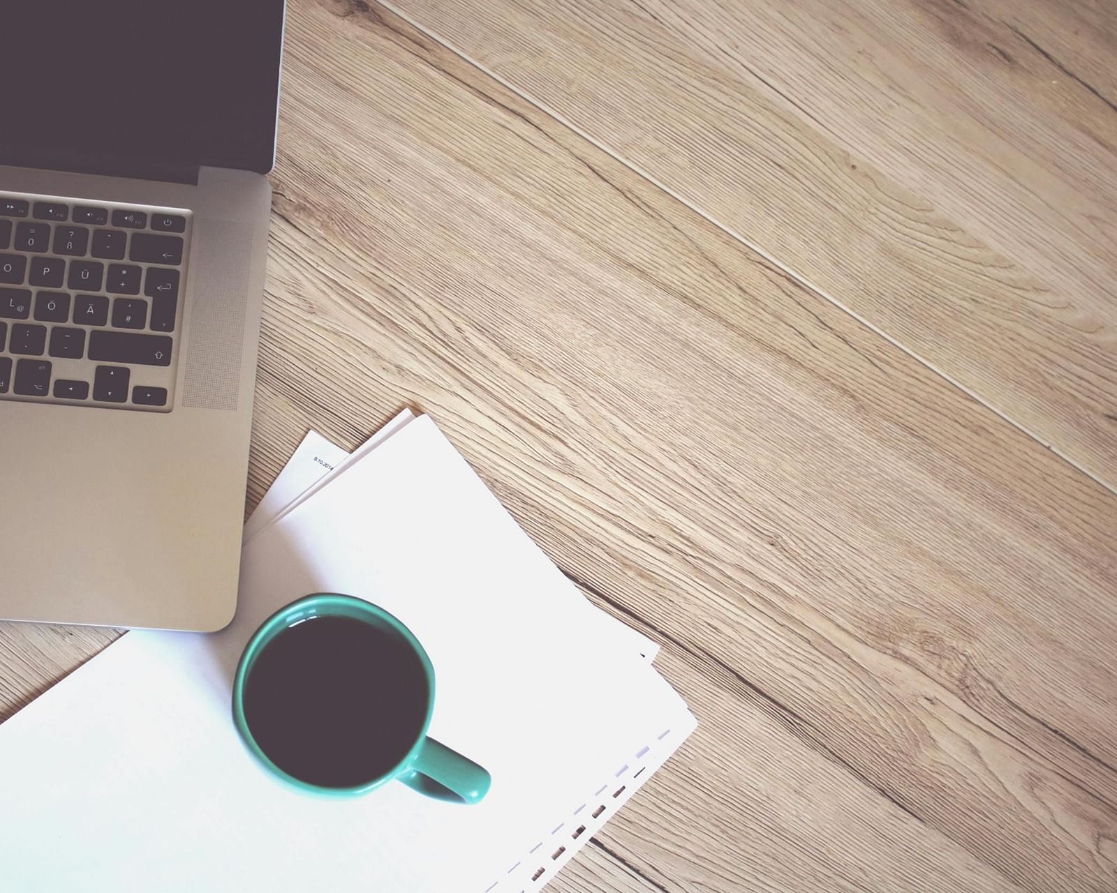 A desk setting with a laptop, papers, and a mug of coffee on a wooden surface.