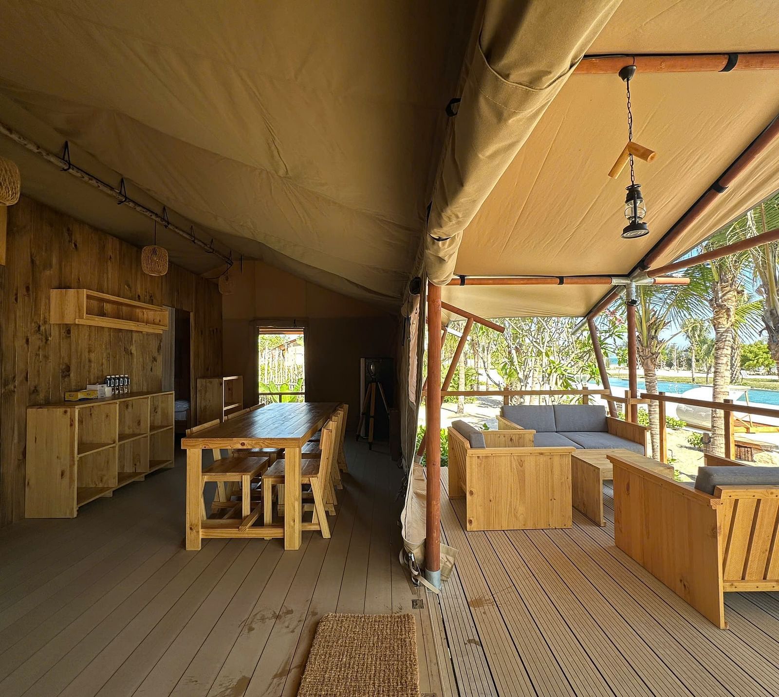 Inside the Grateful Tent at WoCAL Retreat Ke Ga, an open-plan living area includes a handcrafted dining table, cushioned benches, and a view out to tropical greenery through wide tent openings.