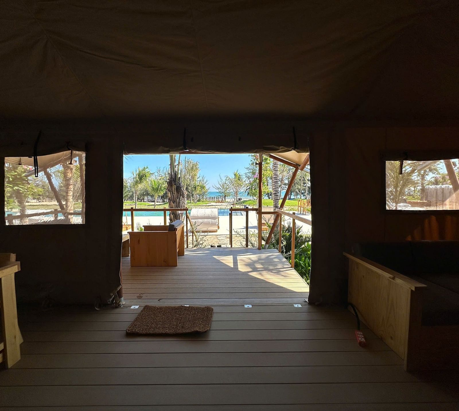 A darker interior view of the Grateful Tent at WoCAL Retreat Ke Ga, looking out through large canvas flaps that open to a private deck, capturing the contrast between cozy shelter and the open outdoors.