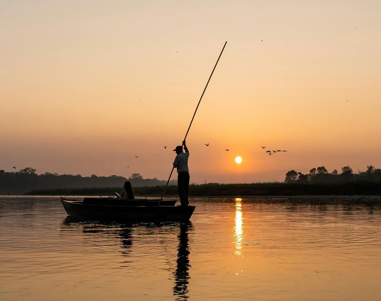 Fisherman on a small boat in a water body during sunset.