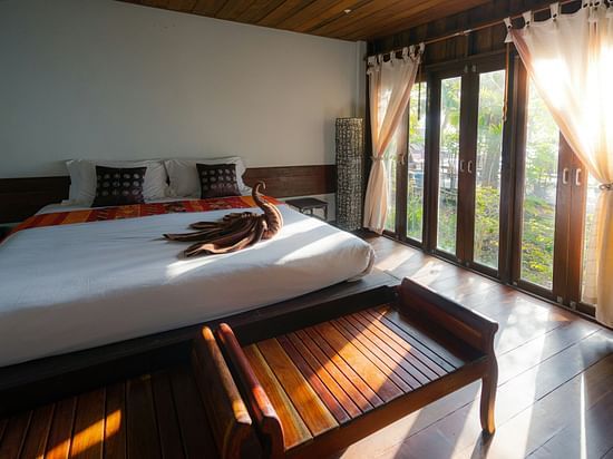 A bedroom featuring a platform bed, sheer curtains, and floor-to-ceiling windows overlooking greenery.