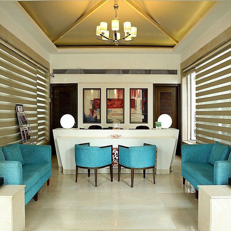 A reception area featuring stylishly arranged furniture, wall-mounted photographs, and a chandelier hanging from the ceiling at Inde Signature Tower, Gurgaon