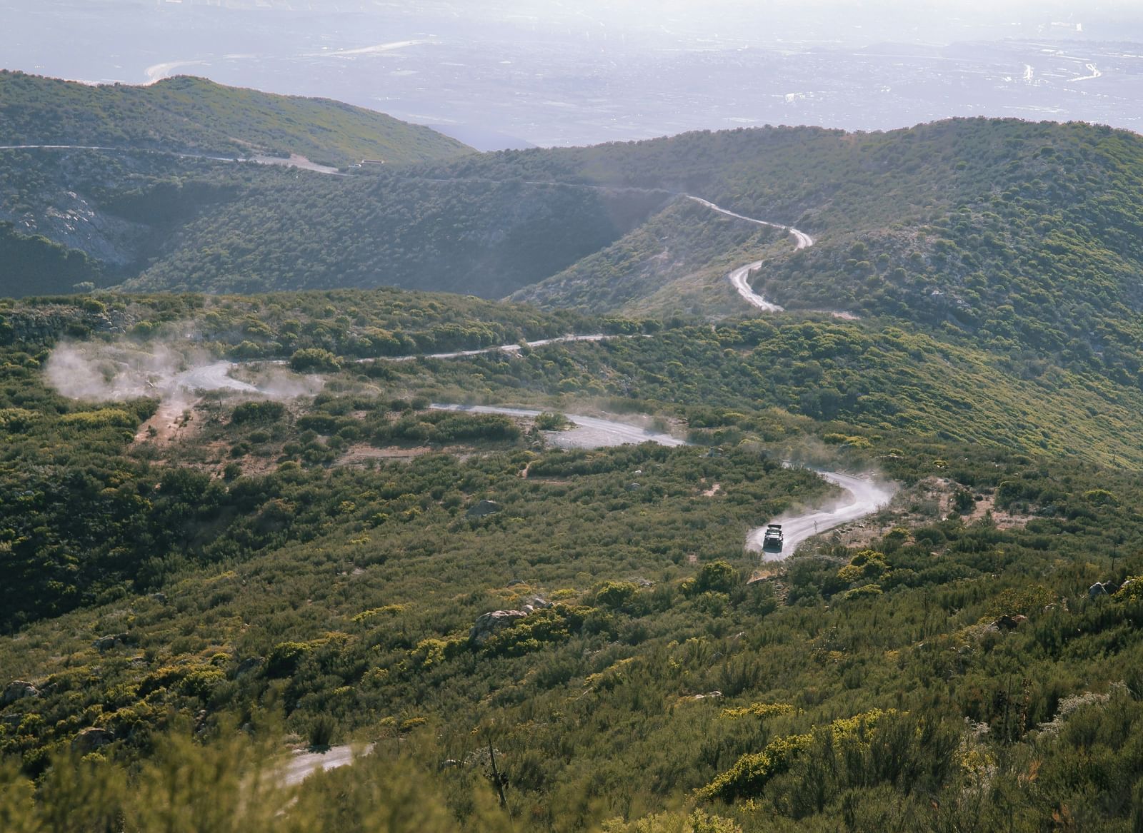 A high-angle view of a winding road traversing a ridge of forested mountains.