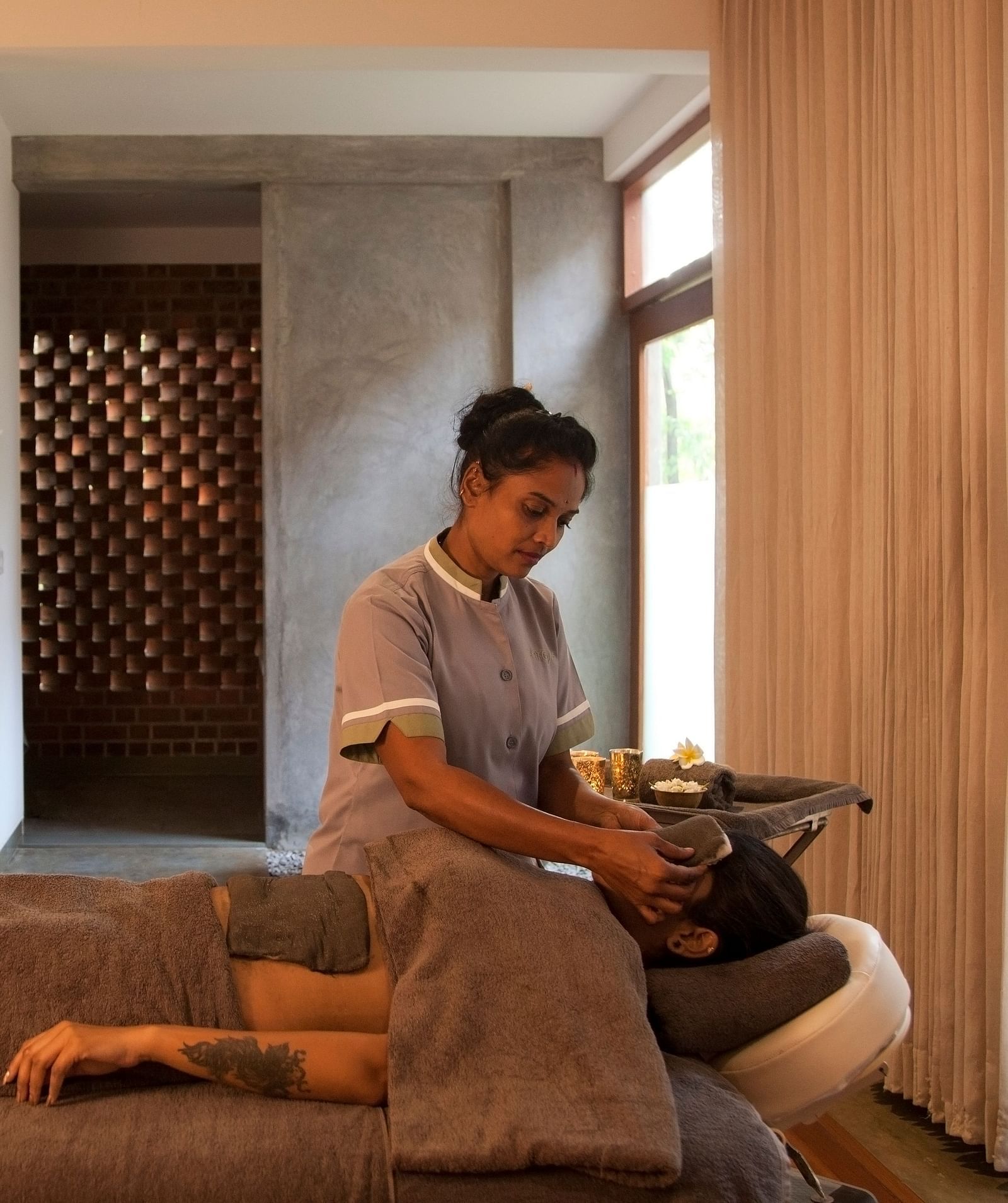 Person receiving head massage on massage table in room with lamp, picture frame, and window - Shreyas Retreat