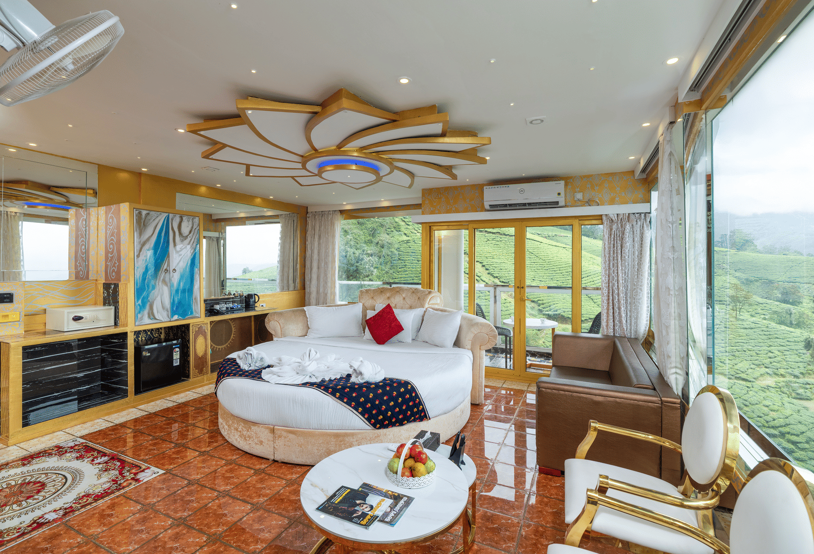 The bedroom of the Jacuzzi 180-degree Suite at Parakkat Nature Hotel and Resorts, Munnar, featuring a large bed, seating, an elaborate ceiling design, and large windows with a view of the surrounding hills.