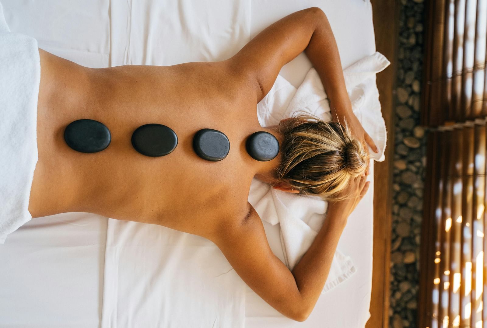 A woman lying down with back with black stones kept over her spine.