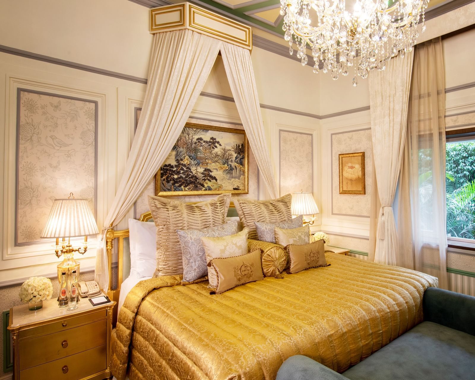 Image of a luxurious bedroom with a golden comforter, neatly arranged pillows, and cushions - The Claridges New Delhi