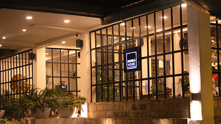 Night view of Sohra House restaurant entrance at Polo Resort Cherrapunji with glass walls, fairy lights, potted plants and warm spotlights.