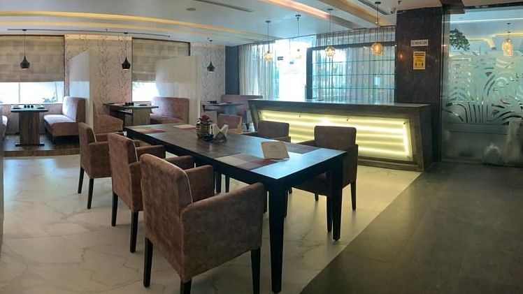 A restaurant interior with a long table, chairs, and soft pink seating, featuring ceiling lights - VITS Gurugram