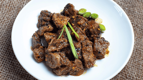 A plate of traditional Newari spiced grilled meat (Choila) served on a rustic burlap background at a restaurant in Kathmandu, Nepal.