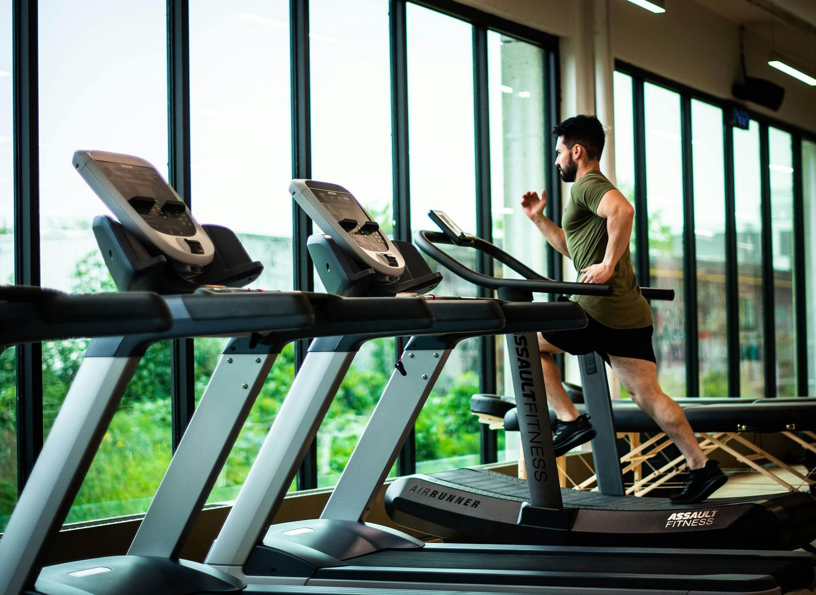 A man running on a treadmill with lush green views outside the huge glass windows.