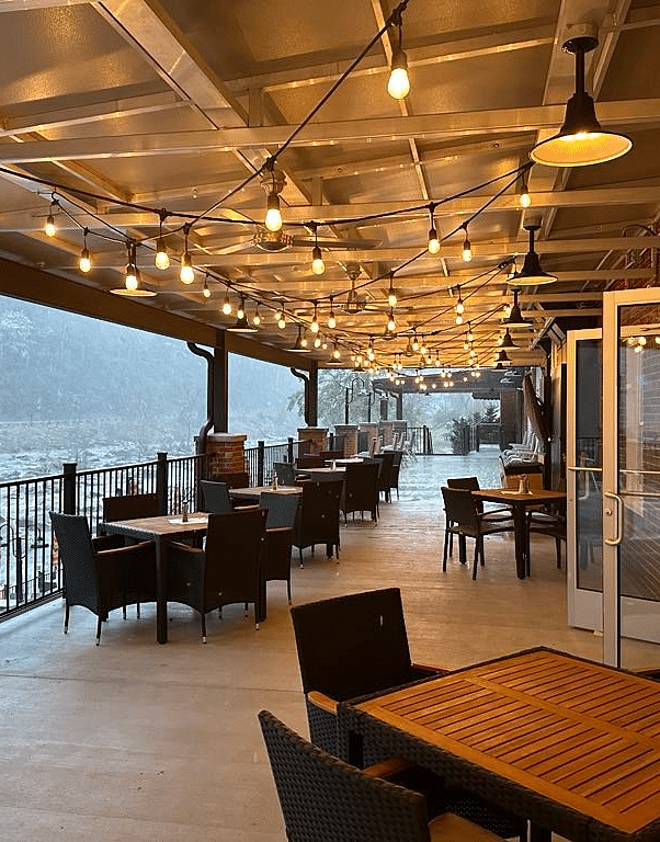 full view image of the cheaoh terrace with warm lighting in the roofed area overlooking the misty river surroundings - Historic Tapoco Lodge